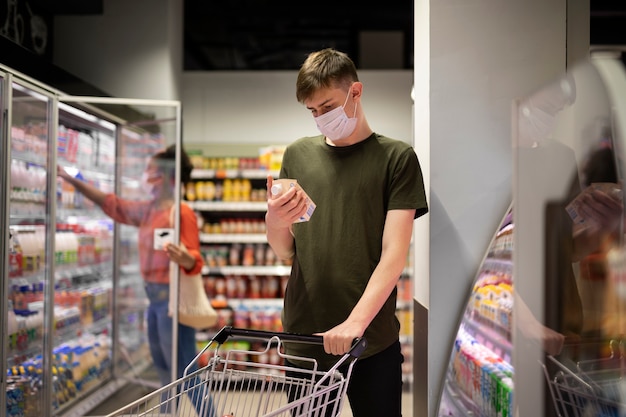 사진 의료용 마스크를 쓴 남녀가 쇼핑 카트를 들고 식료품 쇼핑을 하고 있다