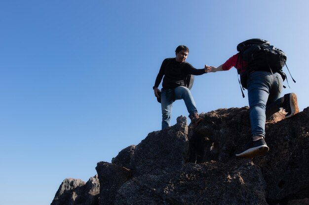 写真 バックパッカーの男と女は山を登っている男は女性を引き上げるために手を伸ばしている