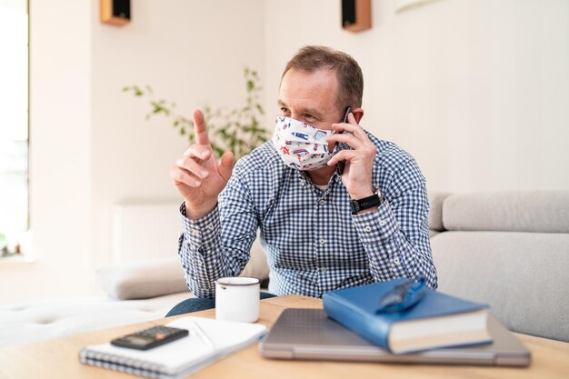 Man in anti bacterial mask on his face talking on cell phone during pandemic Homeoffice businessman talking on phone Freelancer works at home Telephone conversations Distance work