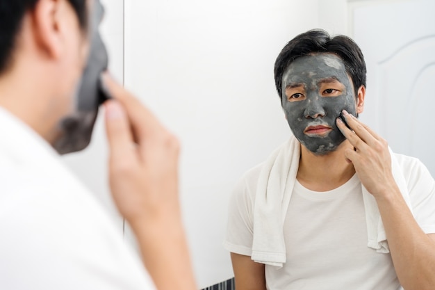 バスルームの鏡に顔のマスクを適用する男