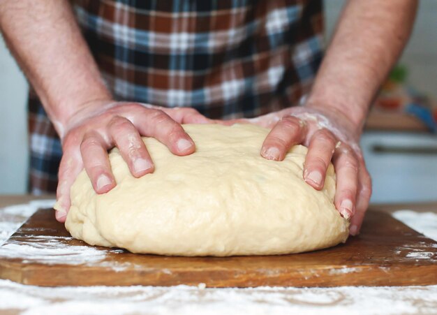 A man in an apron kneads the dough on a wooden board Hands close up