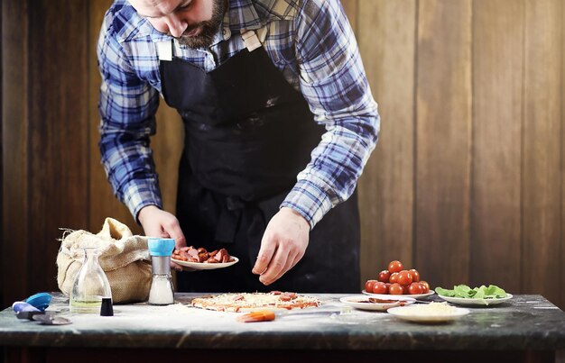 Man in an apron preparing a pizza, knead the dough and puts ingredients