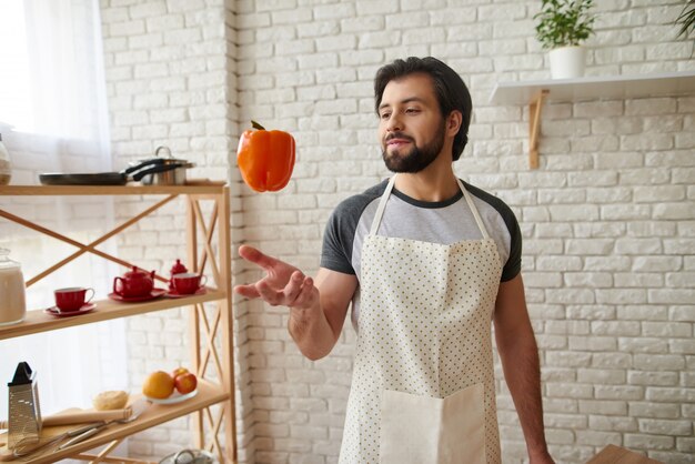 Man in apron tosses up orange pepper into air.