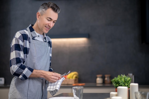 Man in apron wiping cutlery with napkin