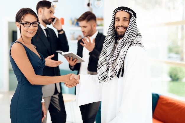 A man in arabian clothes and a girl are shaking hands.