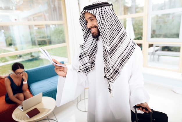 A man in arabian clothes is holding a suitcase.