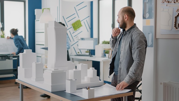 Man architect taking notes on blueprints plan to design building structure and model. Industrial contractor creating construction layout and working on project strategy with maquette.