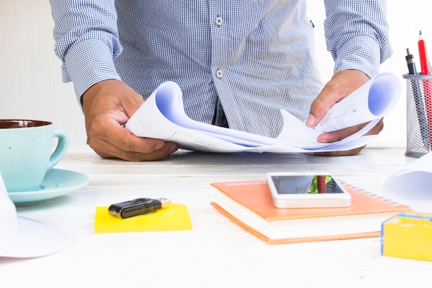 Man architect with  house plans in his hand and equipment on white table