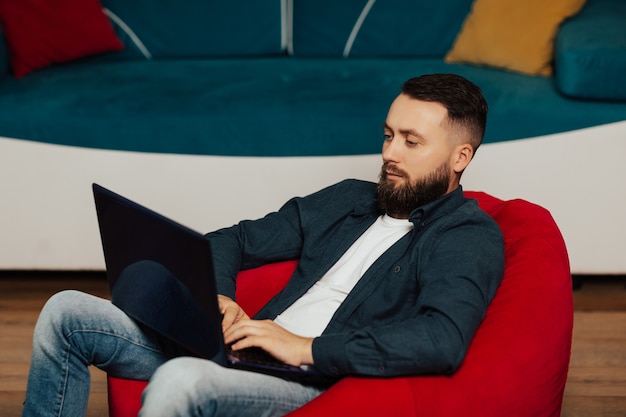 man are using laptop, sitting in cozy red armchair at home.