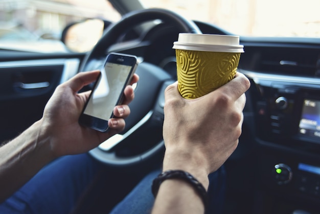 Le braccia dell'uomo tengono un caffè e un telefono in automobile