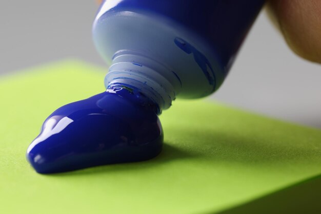 男性アーティストは、緑色の紙にチューブの明るい青色の塗料を絞り出します