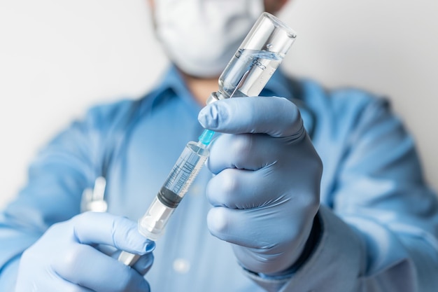 Foto man, arts in blauw shirt en handschoenen, met een spuit en vaccinfles in de hand tegen ziekte coronavirus of griep, vaccinatieconcept.