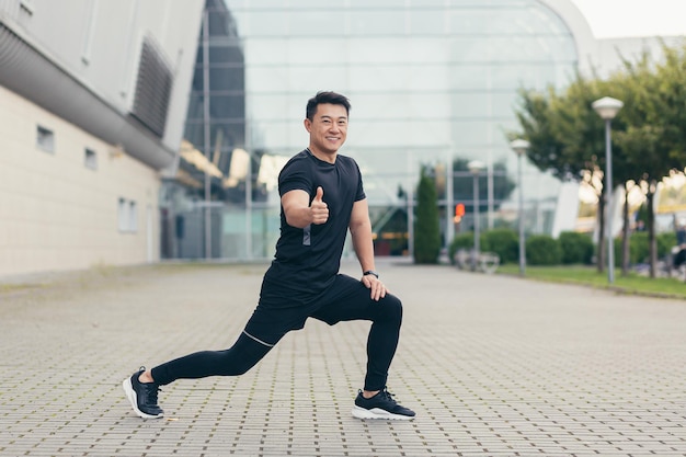 Man asian athlete doing fitness smiling and looking at camera holding outstretched hand and showing thumb up