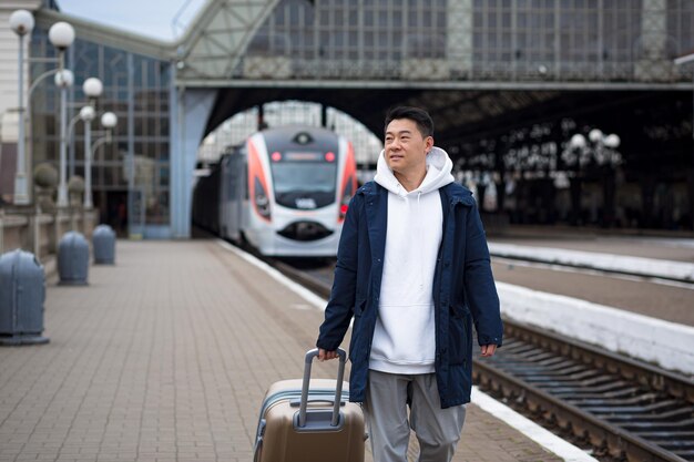 男アジア人の乗客が駅で大きなスーツケースの観光客と一緒にノームの町に到着します