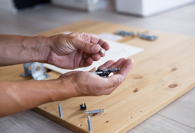 Man assembling furniture at home, male hand with wooden dowel pins and screws.