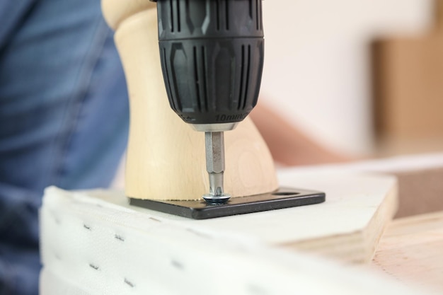 Man assembling sofa furniture at home using cordless screwdriver