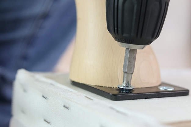 Man assembling sofa furniture at home using cordless screwdriver