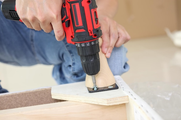 Man assembling sofa furniture at home using cordless screwdriver