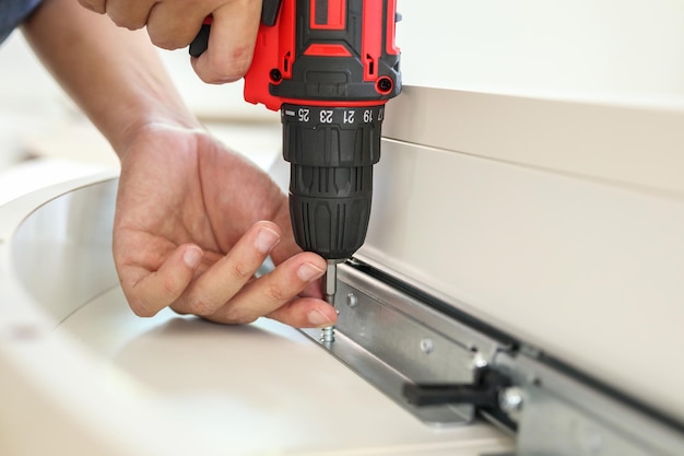 Man assembling white table furniture at home using cordless screwdriver