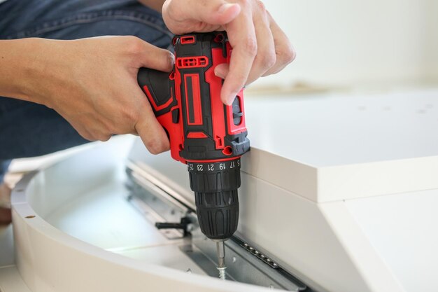 Man assembling white table furniture at home using cordless screwdriver