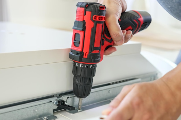 Man assembling white table furniture at home using cordless screwdriver