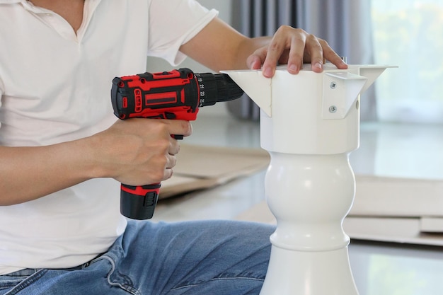 Man assembling white table furniture at home using cordless screwdriver