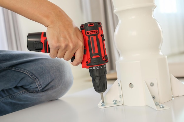 Man assembling white table furniture at home using cordless screwdriver