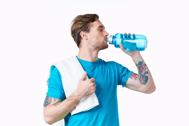 남자 운동 선수 는  바탕 에 있는 병 에서 물 을 마시며 어깨 에 수건 을 고 있다