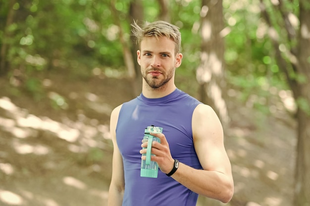 Мужчина-спортсмен держит бутылку для гидратации тела после тренировки Освежающий витаминный напиток после отличной тренировки Спортсмен пьет воду после тренировки в парке Мужчина спортивной внешности держит бутылку с водой
