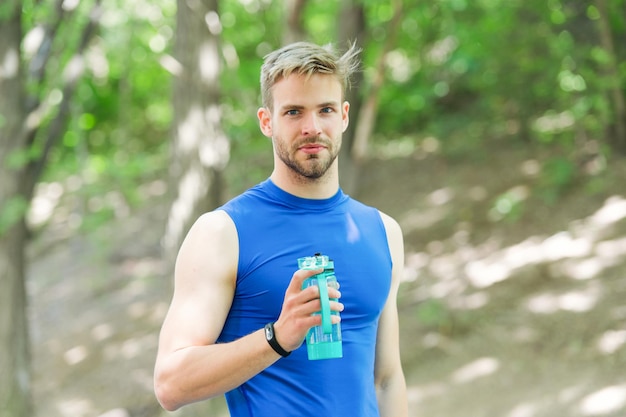 Man athlete hold bottle care hydration body after workout. Refreshing vitamin drink after great workout. Athlete drink water after training in park. Man athletic appearance holds water bottle.