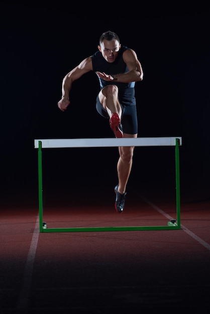 man athlete jumping over a hurdles on athletics race track