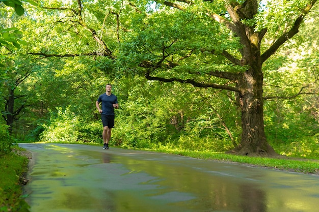 A man athlete runs in the park outdoors around the forest oak trees green grass young enduring