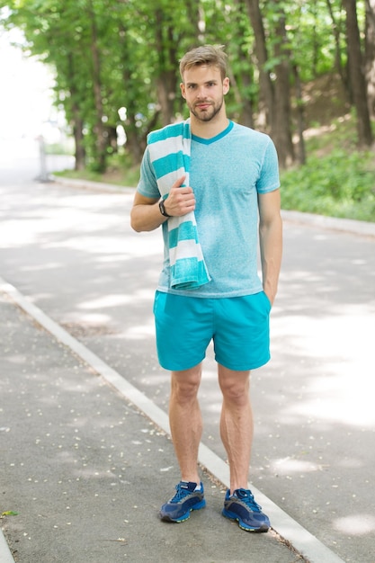 Man athlete with towel after running outdoor nature background athletic man training in park athlete in sport clothes and towel training runner workout on sunny day sport and workout concept