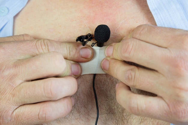 A man attaches a hidden microphone to his chest with an adhesive tape.