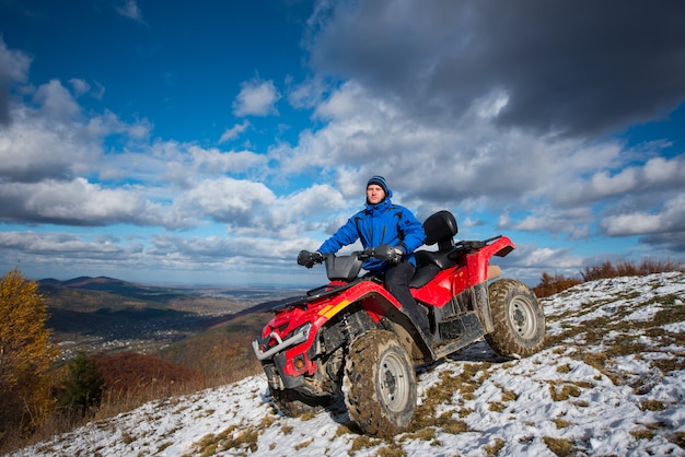 Man on atv riding down from the snow-capped peaks on a sunny day.