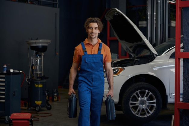 man auto mechanic carrying canisters with car motor oil