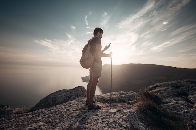 Man backpacker met smartphone ontspannen op de bergtop alleen reizen. levensstijl actieve vakanties moderne technologie millennials concept. Prachtige dageraad. mock-up tekst.