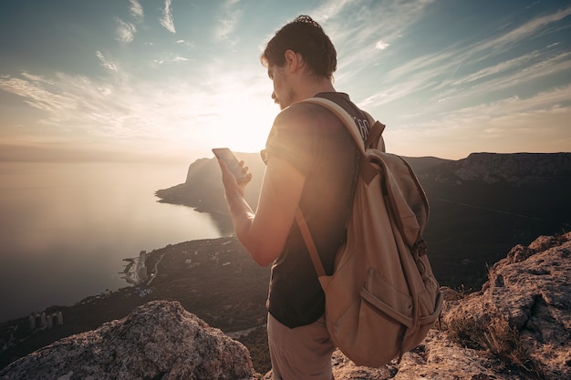 Man backpacker met smartphone ontspannen op de bergtop alleen reizen. levensstijl actieve vakanties moderne technologie millennials concept. prachtige dageraad. mock-up tekst.