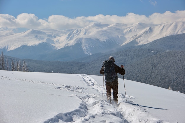 Man backpacker wandelen besneeuwde berghelling op koude winterdag.