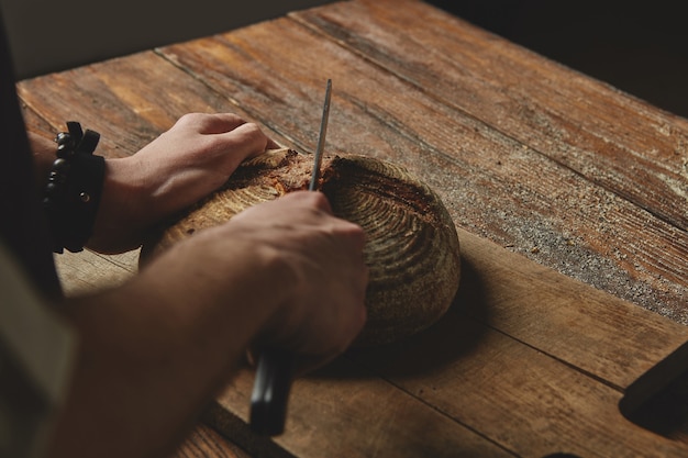 오래 된 나무 배경에 나무 커팅 보드에 칼 빵을 자르는 남자 베이커