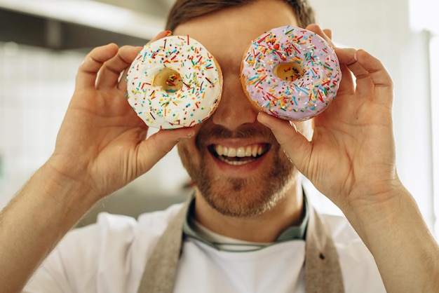 Photo man baker having fun with donuts and smiling