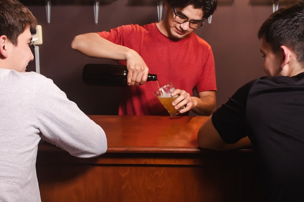 Мужчина в баре подает своим счастливым клиентам стакан пива.