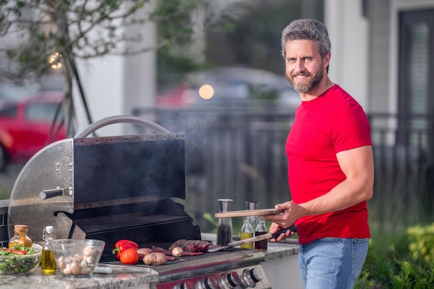 man at a barbecue grill male cook preparing barbecue outdoors bbq meat grill roasted beef attractive man preparing barbeque in the house yard barbecue and grill cook cooking barbecue steak
