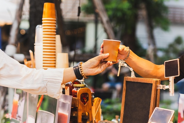 Man barista serving hot coffee in paper cup to customer over counter in cafe outdoor