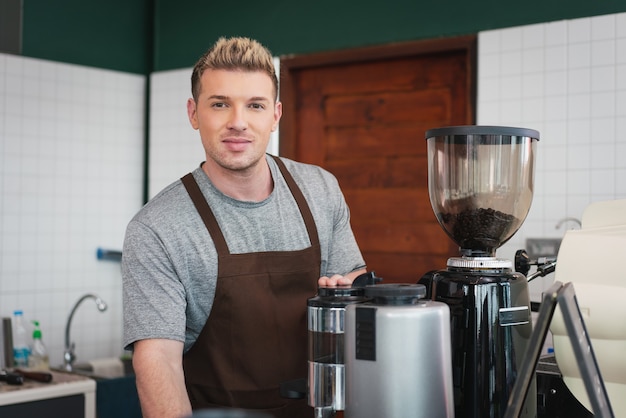 コーヒー ショップのコーヒー マシンの後ろに立っている男性バリスタ