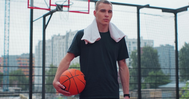 カメラを見て遊び場にボールを持つ男性バスケットボール選手健康的なライフスタイルとスポーツのコンセプト
