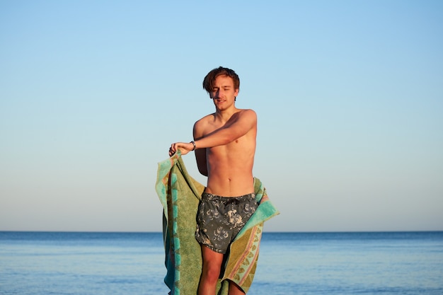 A man on the beach drying himself with a green towel