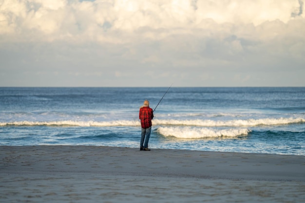 man beach fishing in the ocean waves at dusk on a holiday