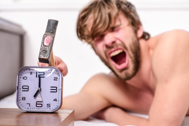 Man bearded annoyed sleepy face lay pillow near alarm clock\
break discipline regime stop ringing annoying sound annoying\
ringing alarm clock guy knocking with hammer alarm clock\
ringing