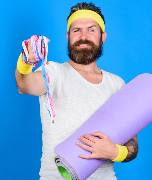 Man bearded athlete hold fitness mat and tape measure. Athlete guide stay in shape. Old school aerobics concept. Athlete professional coach motivated for training. Athlete wear bandages for sweat.